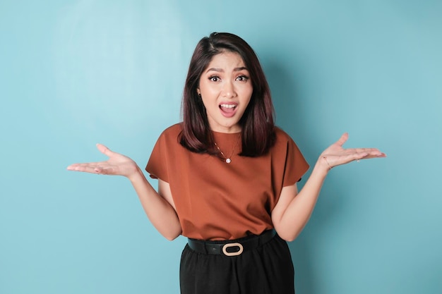 Un portrait d'une femme asiatique portant une chemise marron a l'air si confus isolé par un fond bleu