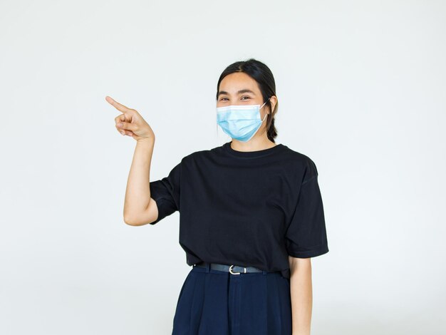 Portrait d'une femme asiatique portant un masque facial, pointant une publicité sur fond blanc, espace de copie vierge avec découpe de fond blanc isolé.