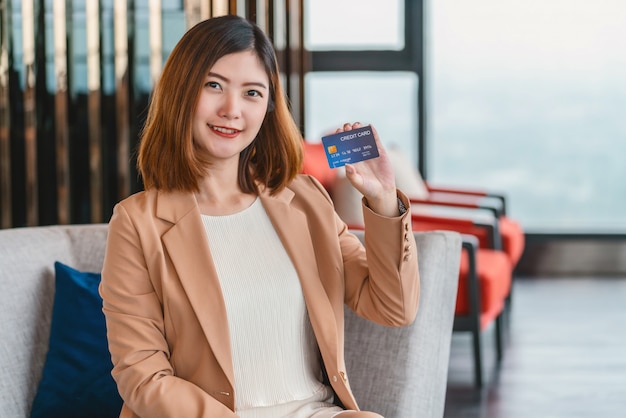 Portrait femme asiatique présentant la carte de crédit pour les achats en ligne dans un hall d'accueil moderne ou un espace de travail