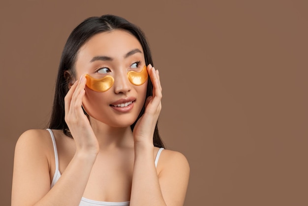 Portrait d'une femme asiatique séduisante portant de l'or sous des pansements oculaires regardant de côté l'espace libre sur