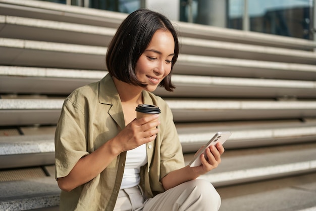 Portrait de femme asiatique avec smartphone boit du café et regarde des vidéos sur téléphone mobile fille avec t