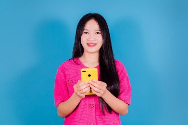 Portrait d'une femme asiatique souriante à l'aide d'un smartphone sur fond bleu