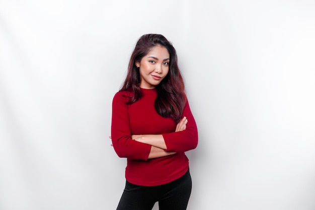 Portrait d'une femme asiatique souriante confiante vêtue de rouge debout avec les bras croisés et regardant la caméra isolée sur fond blanc