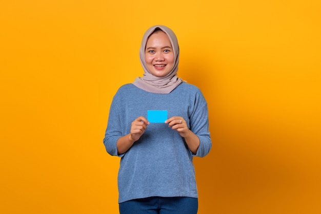 Portrait de femme asiatique souriante debout et tenant une carte de crédit sur fond jaune