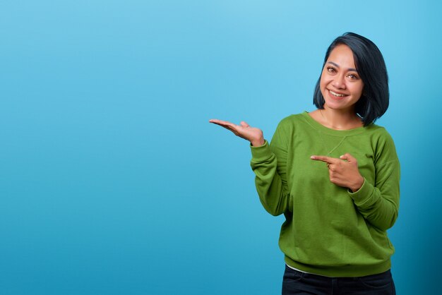 Portrait de femme asiatique souriante montrant le produit sur fond bleu