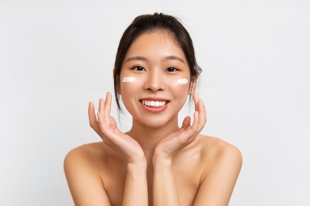 Portrait de femme asiatique touchant l'application de crème sur les joues
