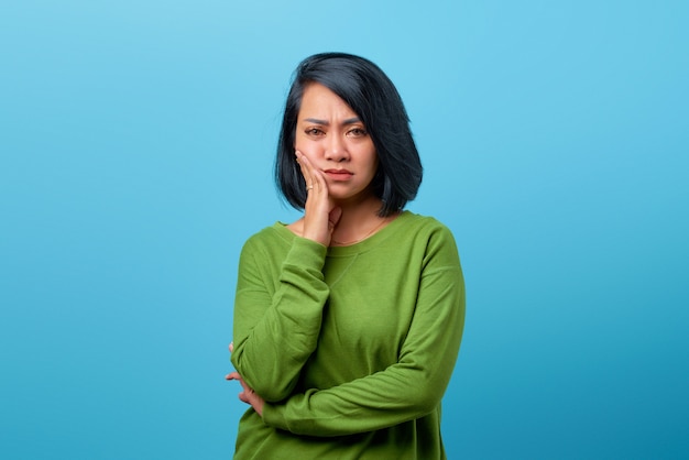 Portrait d'une femme asiatique touchant la joue avec une expression ennuyée sur fond bleu