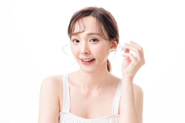 Portrait d'une femme asiatique avec un visage éclatant et une peau douce et propre appliquer du sérum avec une pipette Modèle féminin avec un maquillage naturel en studio Cosmétologie Traitement du visage Thérapie et concept de spa