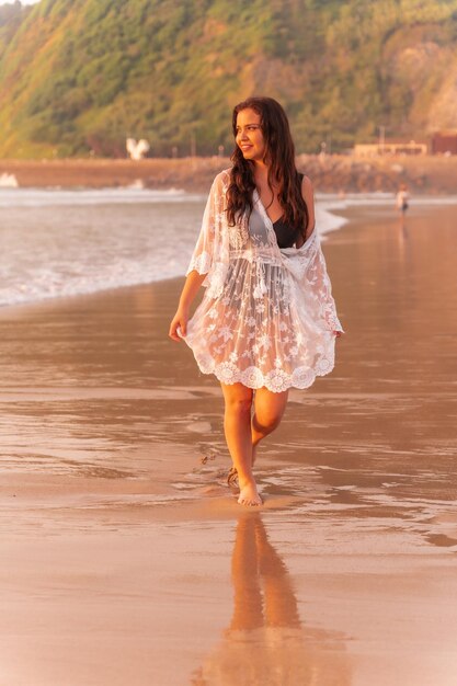 Portrait d'une femme au coucher du soleil dans une robe blanche profitant de vacances sur la plage