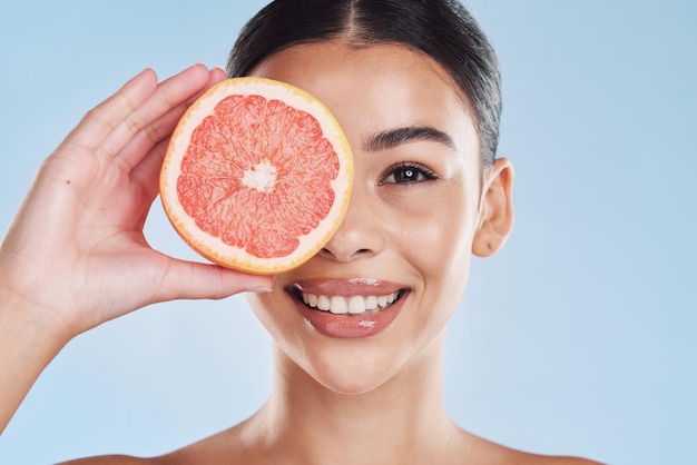 Portrait d'une femme au visage heureux et au pamplemousse sur fond de studio bleu Sa routine de soins de la peau et de bien-être garde son corps frais ou sain, son hygiène dentaire et son sourire propre ou ses dents blanches