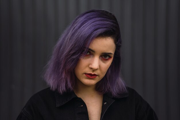 Portrait d'une femme aux cheveux violets et rouge à lèvres rouge sur fond de mur noir