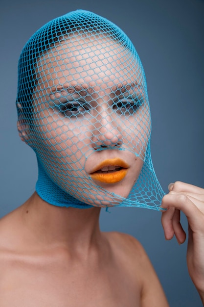 Portrait de femme avec un bas bleu déchiré sur la tête sur fond bleu. Rouge à lèvres jaune