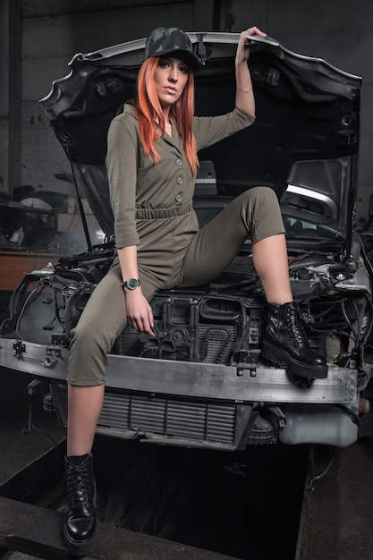 Portrait d'une femme de beauté en jeans court et haut sur fond d'atelier. Modèle de fille en tenue attrayante avec voiture démontée dans le garage.