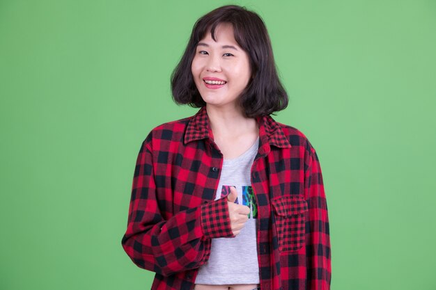 Portrait de femme belle hipster asiatique aux cheveux courts contre clé chroma ou mur vert