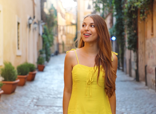 Portrait de femme belle mode aux cheveux longs en robe d'été jaune à pied et à la découverte du quartier de Trastevere à Rome, Italie.