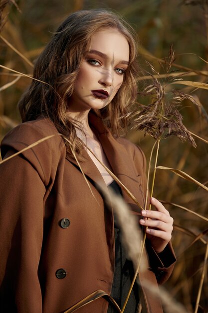 Portrait d'une femme belle mode dans un fourré d'herbe d'automne