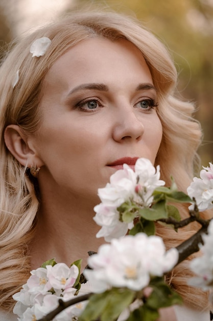 Portrait de femme blonde adulte appréciant l'arbre en fleurs dans le jardin de printemps