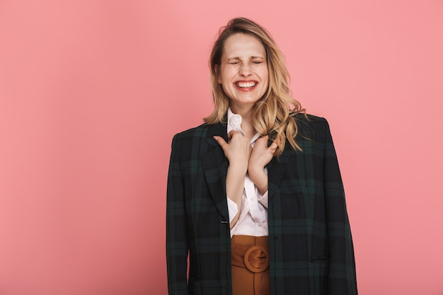 Portrait de femme blonde des années 30 en veste tendance souriante et posant isolée sur rose