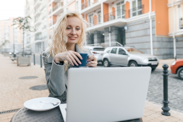 Portrait de femme blonde dans un café en plein air avec ordinateur portable
