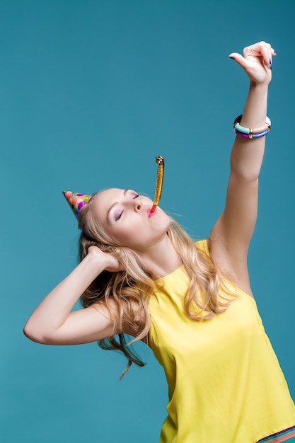 Portrait de femme blonde drôle en chapeau d'anniversaire et chemise jaune sur fond bleu célébration et fête