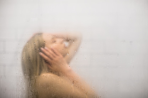 Portrait de femme blonde sous la douche derrière une vitre avec des gouttes