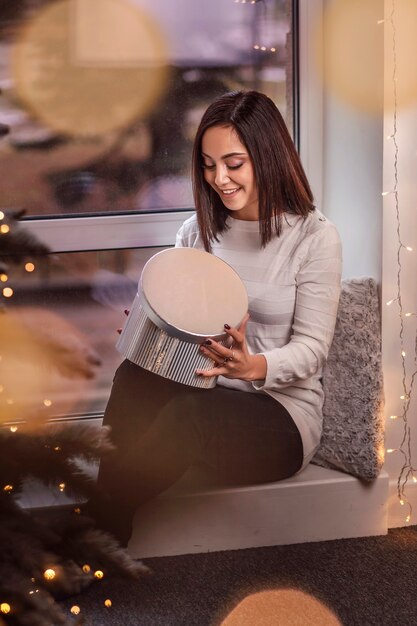 Portrait d'une femme avec une boîte-cadeau dans ses mains sur un fond de guirlande de Noël