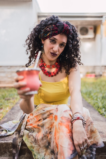 Portrait d'une femme avec des boucles buvant du thé mate.