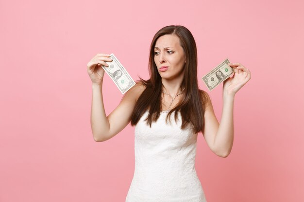 Portrait de femme bouleversée dégoûtée en robe blanche à la recherche de billets d'un dollar