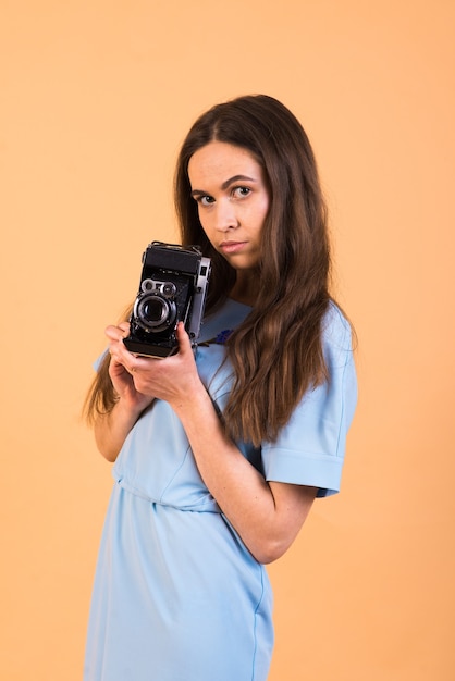 Portrait de femme brune avec un appareil photo à la main sur un mur jaune. Isolé .