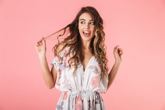 Portrait de femme brune aux cheveux longs portant une robe souriant à la caméra, isolé sur rose