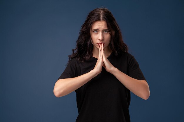 Portrait d'une femme brune aux cheveux longs en t-shirt noir posant sur fond gris et montrant différentes émotions.