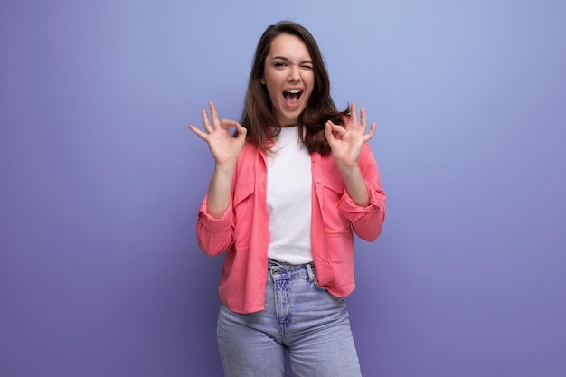 Portrait d'une femme brune en chemise et jeans posant avec un sourire sur un fond de studio