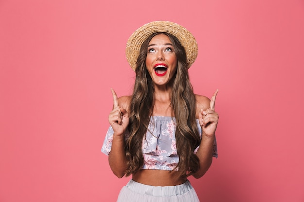 Portrait de femme brune heureuse portant un chapeau de paille hurlant et pointant les doigts vers le haut