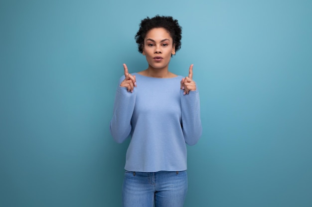 Portrait d'une femme brune latine pleine d'espoir aux cheveux bouclés dans des vêtements décontractés élégants bleus avec les doigts