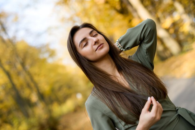 Portrait de femme brune en robe verte posant dans le parc d'automne