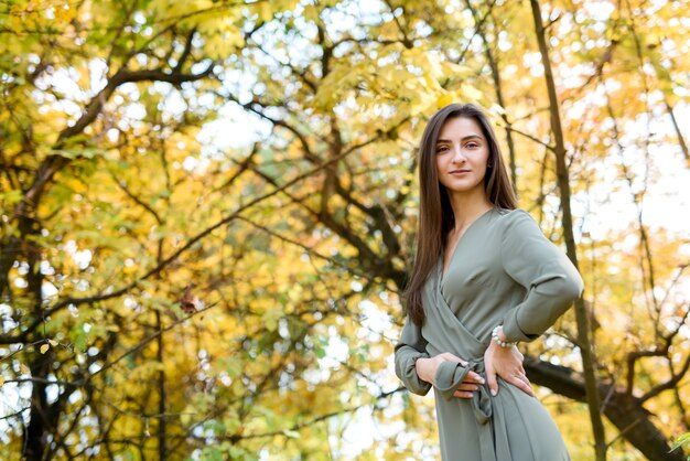 Portrait de femme brune en robe verte posant dans le parc d'automne