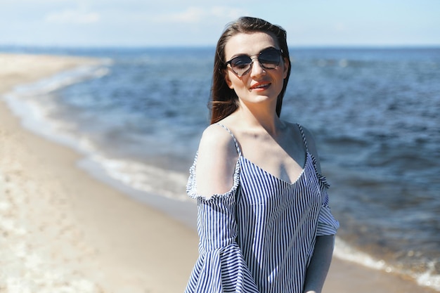 Portrait d'une femme brune souriante et heureuse, debout sur la plage de l'océan et regardant la caméra