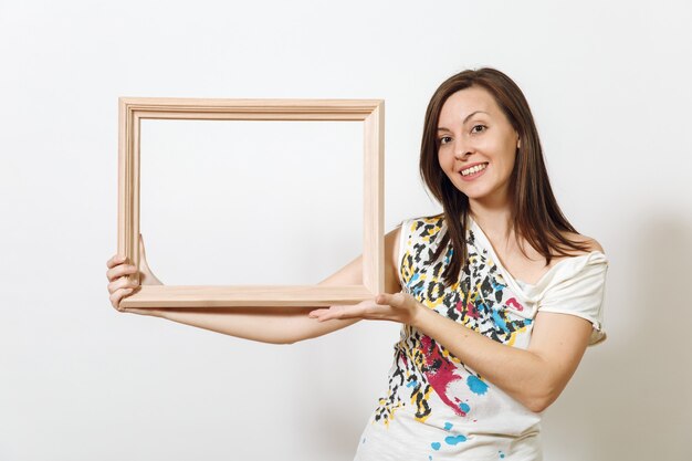 Le portrait d'une femme brune souriante heureuse debout et tenant un cadre en bois vide sur fond blanc. Avec place pour le texte pour la publicité.