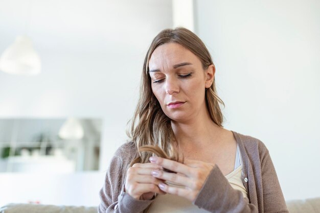 Photo portrait d'une femme brune triste tenant une section sèche de cheveux et regardant les pointes coupées de ses cheveux concept de perte de cheveux et de dommages aux cheveux