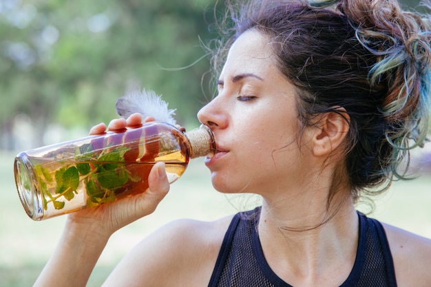 Portrait de femme buvant de l'eau douce à l'extérieur. Jeune femme avec des vêtements de yoga tenant une boisson détox pour nettoyer le corps après avoir fait de l'exercice. Mode de vie sain pour les personnes en été.