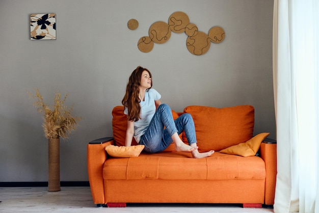 Portrait d'une femme sur le canapé orange dans la salle de repos posant inchangée