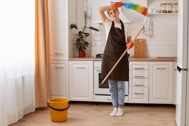 Photo portrait d'une femme caucasienne fatiguée lavant le sol en essuyant son front à la cuisine faisant le ménage à la maison gardant sa maison bien rangée se sentant surmenée regardant la caméra avec une expression épuisée