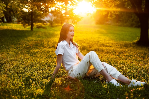 Portrait de femme chaleureuse sur le coucher du soleil assis sur l'herbe