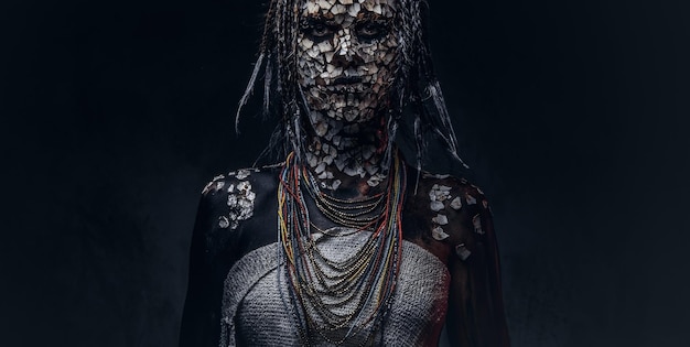 Portrait d'une femme chaman africaine effrayante avec une peau fissurée pétrifiée et des dreadlocks sur fond sombre. Notion de maquillage.