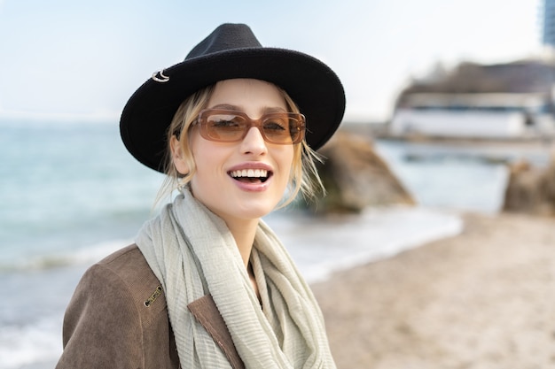 Portrait d'une femme charmante avec un grand sourire portant un chapeau et des lunettes sur la plage