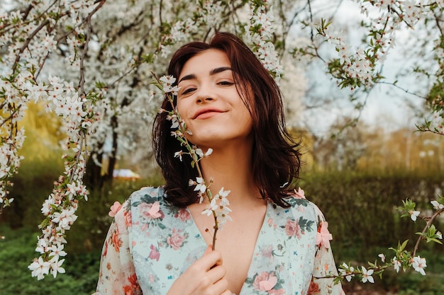 Portrait d'une femme charmante posant près de fleurs de cerisier de pommier en fleurs dans le jardin