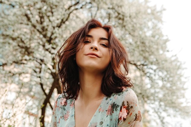 Portrait d'une femme charmante posant près de fleurs de cerisier de pommier en fleurs dans le jardin