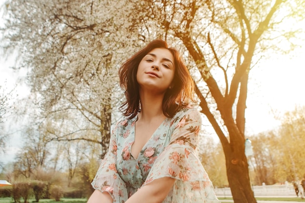 Portrait d'une femme charmante posant près de fleurs de cerisier de pommier en fleurs dans le jardin