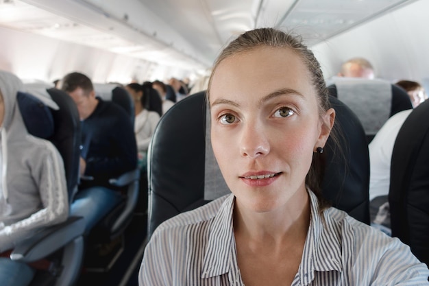 Portrait de femme en chemise posant sur le siège sur fond d'avion avec des passagers.