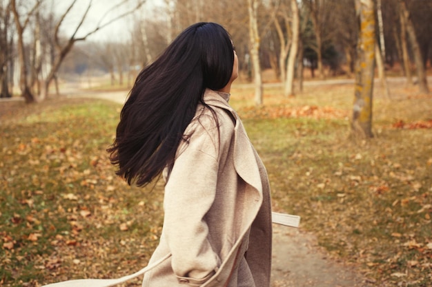 Portrait de femme cheveux brune en manteau beige marchant dans le parc de la ville